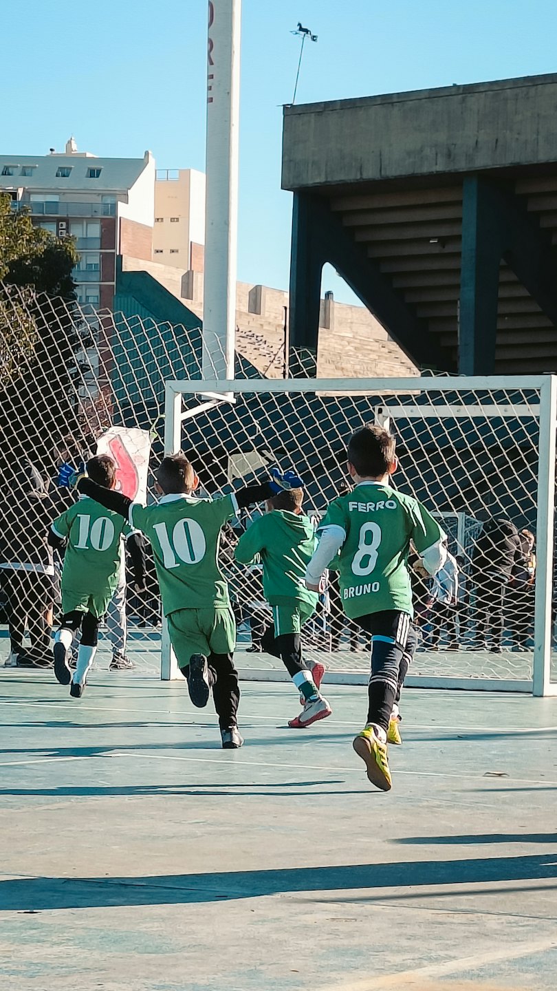 Quattro bambini in maglia da calcio corrono verso una porta.