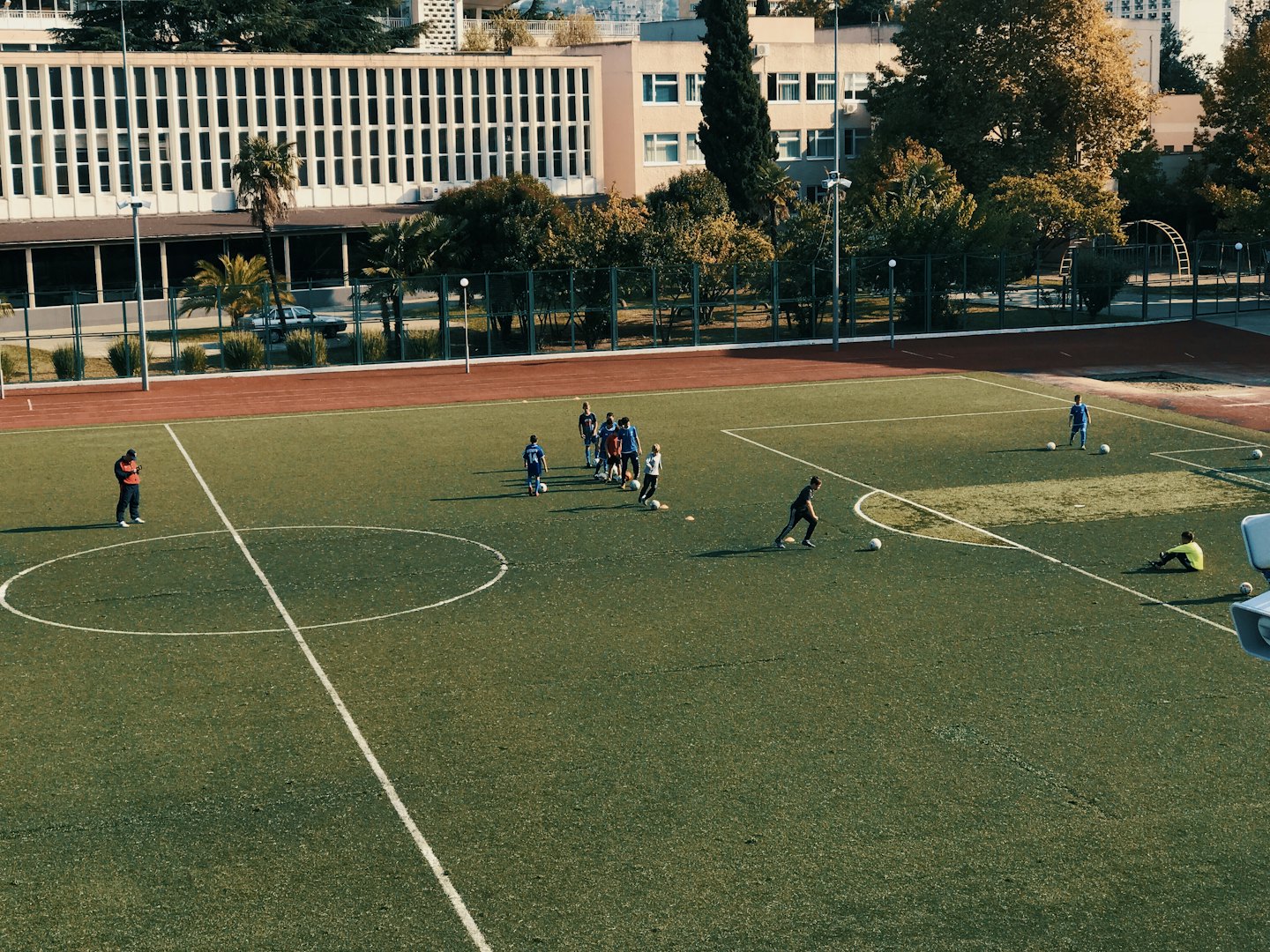 Uomini e ragazzi giocano a calcio su un campo luminoso in erba sintetica.